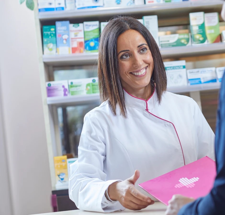 Una farmacéutica entrega una carpeta a una clienta en el mostrador